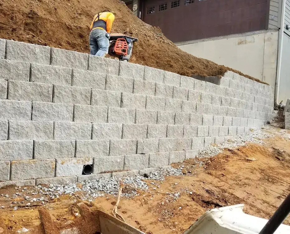 Segmental retaining wall under construction with visible drainage outlet and compacted gravel base in Cincinnati, Ohio.